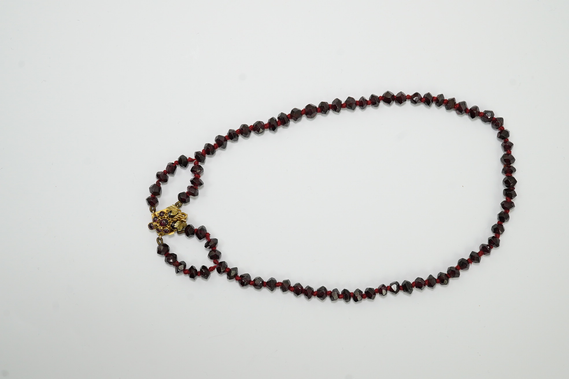 A Victorian facet cut garnet necklace, with cabochon garnet cluster set gold clasp